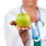 Close-up of a doctor presenting a green apple against a white background